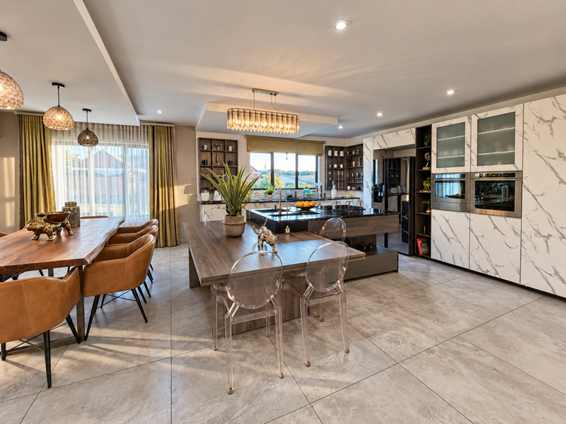 A modern open-plan kitchen and dining area featuring marble-effect cabinetry, a large central island, built-in double ovens, and high-quality tiled flooring.