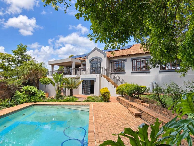 Rear view of the property featuring a swimming pool, brick patio, raised garden beds, and an elevated balcony with wrought iron staircase access.