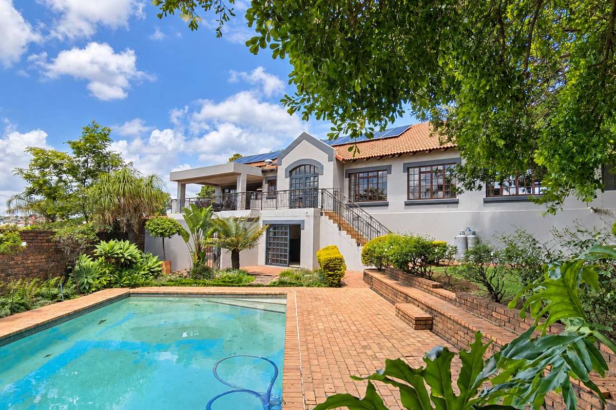 Rear view of the property featuring a swimming pool, brick patio, raised garden beds, and an elevated balcony with wrought iron staircase access.