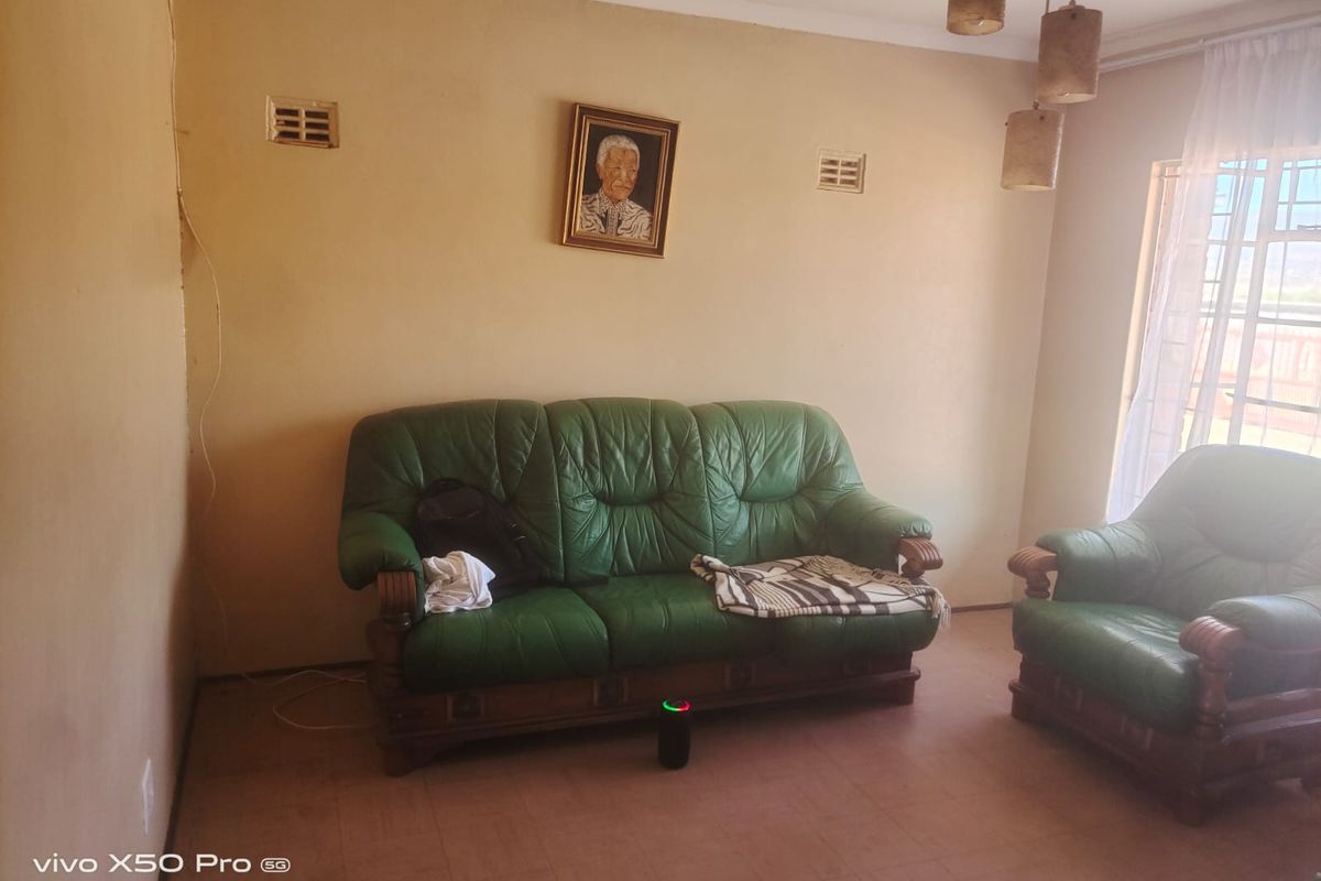 A living room featuring tiled flooring and ventilation grilles, currently showing signs of wear including cracked wall paint and exposed wiring.
