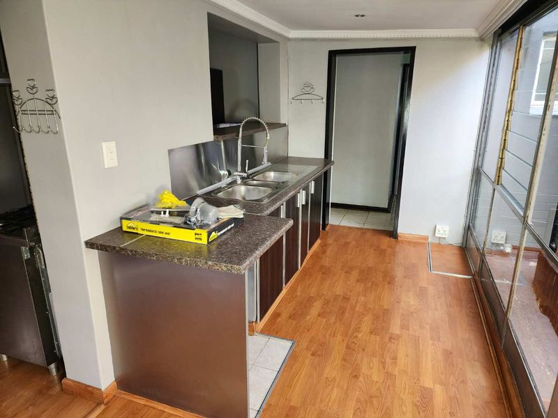 A functional scullery area featuring a double sink, laminate countertops, dark cabinetry, and wood-look flooring, providing a practical space for kitchen preparation and wash-up.
