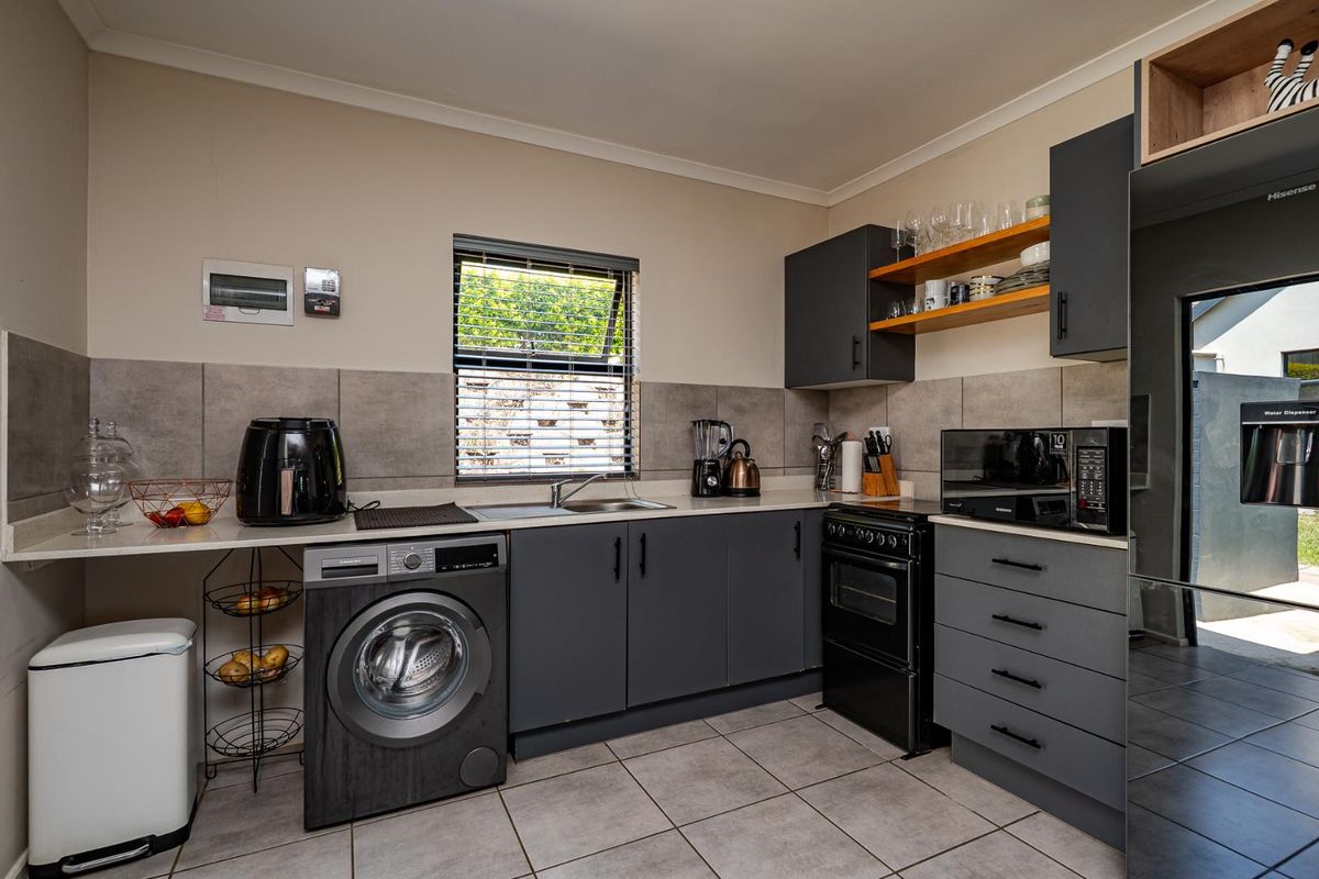 Modern kitchen featuring dark grey cabinetry, stone-look countertops, tiled backsplash, integrated sink, and space for a washing machine.