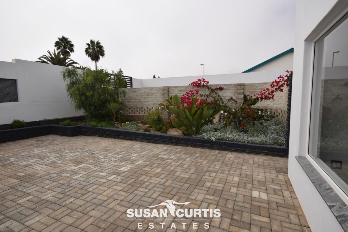 A well-maintained paved courtyard area featuring a raised garden bed with established plantings and a perimeter boundary wall.