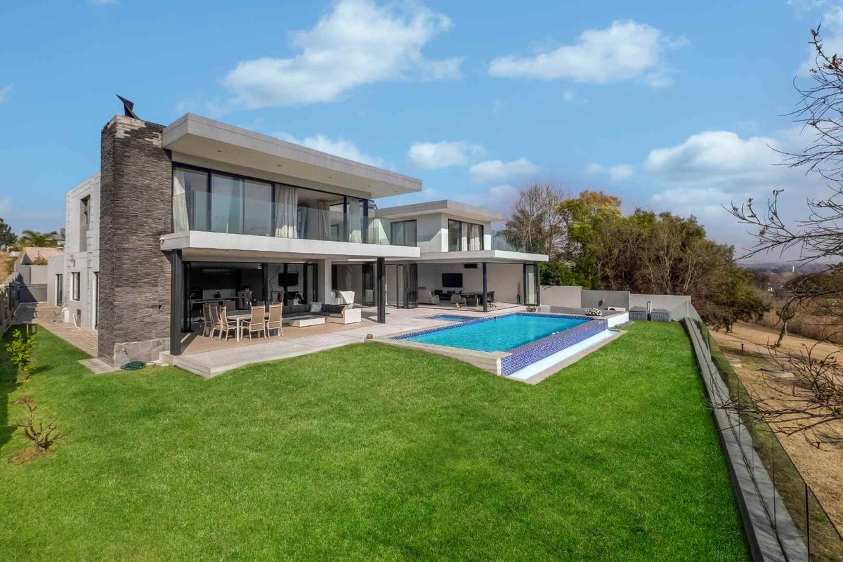 Modern double-story residence featuring a spacious covered patio, swimming pool, and landscaped garden with contemporary stone cladding and expansive glass sliding doors.