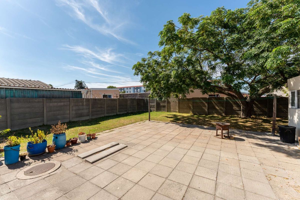 A spacious rear garden featuring a paved patio area, established tree, and perimeter boundary walling, offering a private outdoor space.