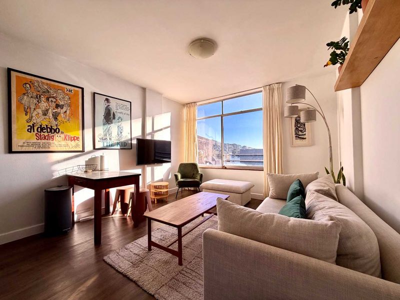 A bright and well-maintained living room featuring large windows that provide ample natural light and views, complemented by modern laminate flooring.