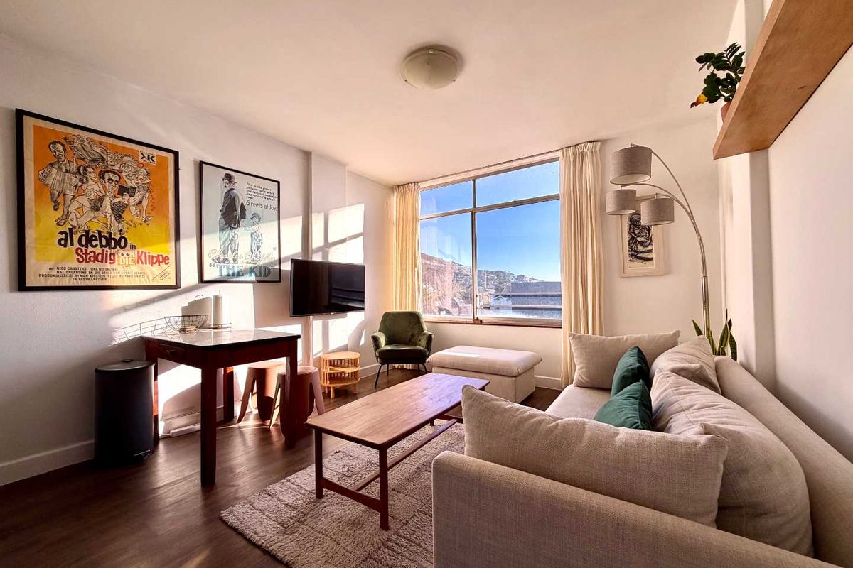 A bright and well-maintained living room featuring large windows that provide ample natural light and views, complemented by modern laminate flooring.