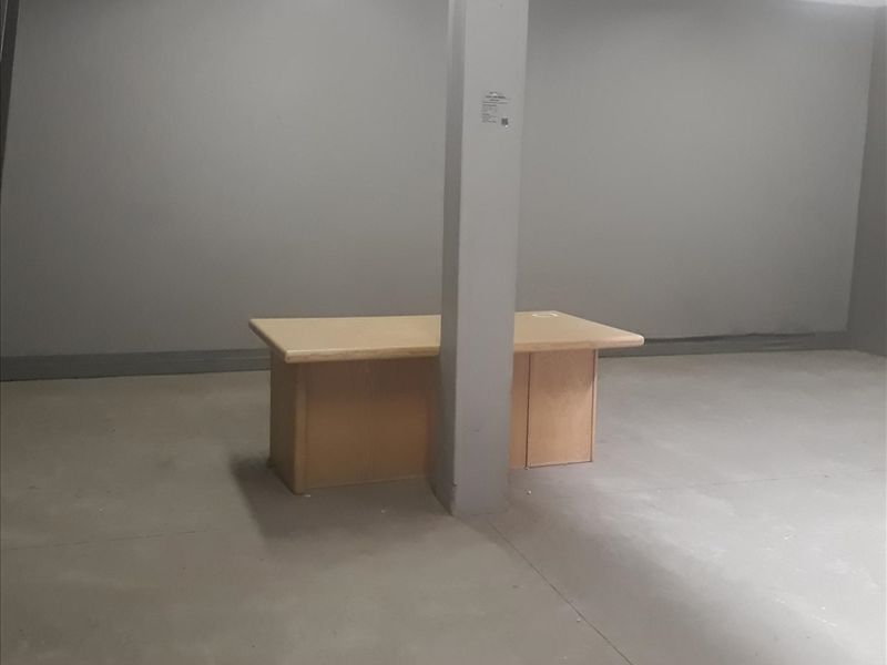 An open-plan industrial office space featuring a central structural support column, fluorescent lighting, and concrete flooring.