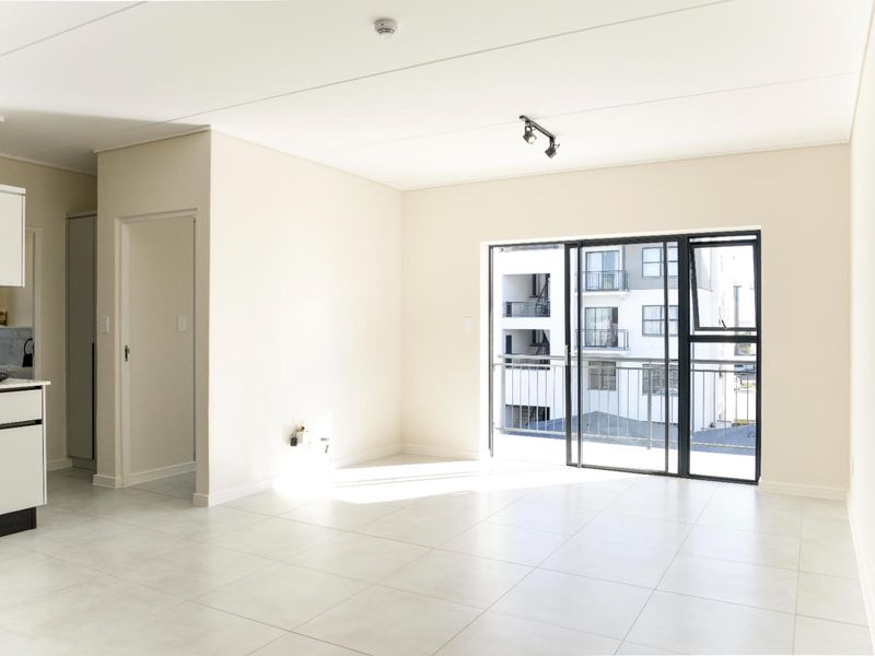 Bright open-plan living area featuring modern tiled floors, a compact kitchen with built-in appliances, and a sliding door leading to a private balcony.