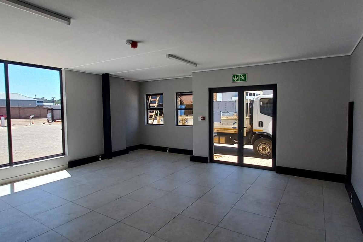 A bright, modern, and empty office space featuring large windows, tiled flooring, and glass panel double doors, suitable for a professional workspace.