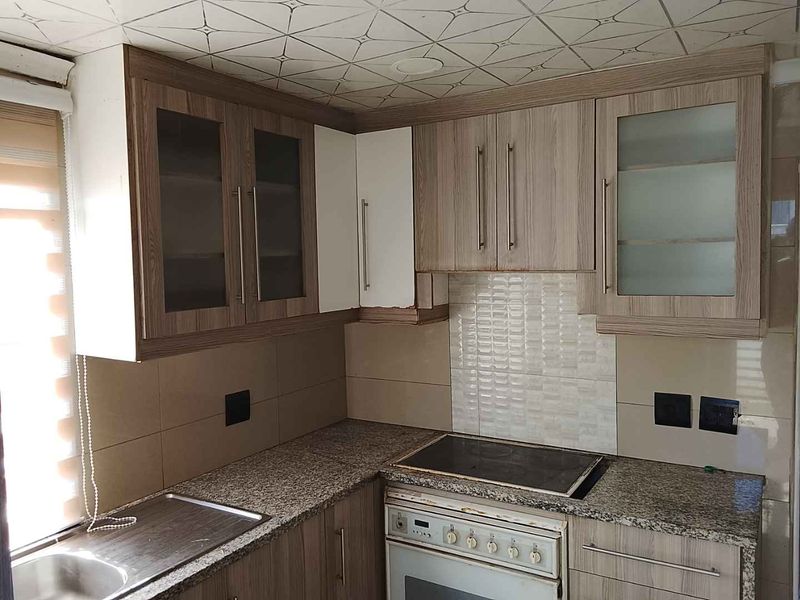 A compact kitchen featuring wood-look laminate cabinetry, granite countertops, a built-in oven with electric hob, and a tiled backsplash.