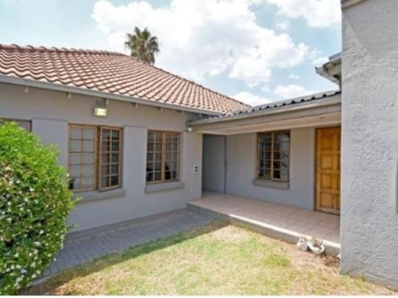 Rear view of the property featuring a paved patio area, tiled roof, and a combination of timber and glass block window detailing.