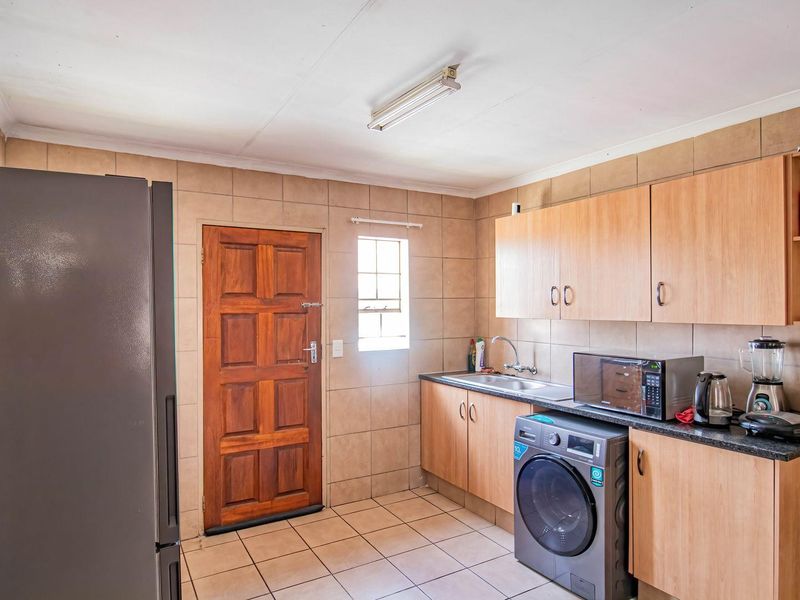 Functional kitchen featuring tiled walls and flooring, built-in wooden cabinetry, laminate countertops, and a stainless steel sink with direct exterior access.