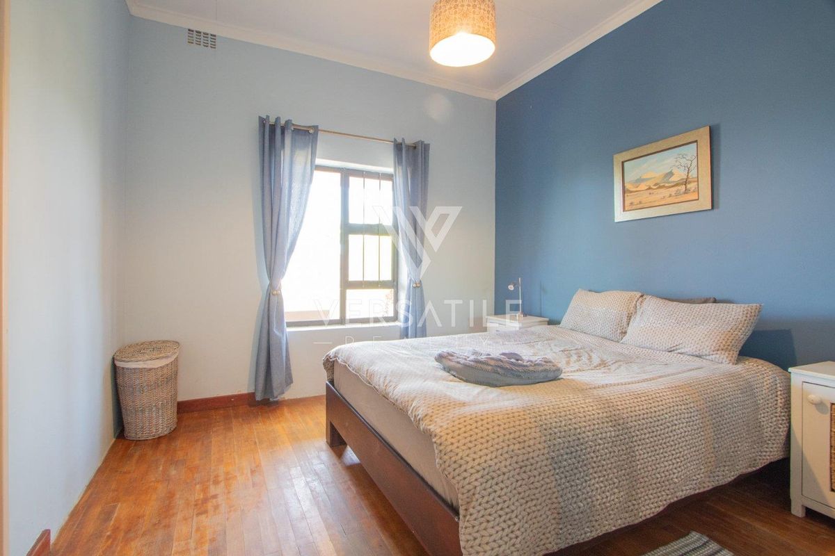 A bedroom featuring timber flooring, a feature wall, and a window with security bars.