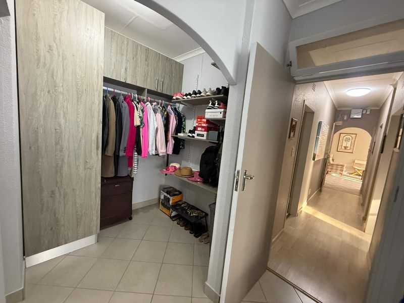 A functional bedroom featuring built-in cupboards with wood-grain finish, tiled flooring, and an arched entryway leading to a connecting hallway.