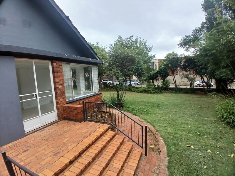 A rear view of the property featuring a brick patio with steps, metal railings, and access to the garden through sliding glass doors.