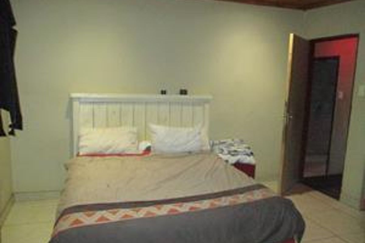 A bedroom featuring tiled flooring and a timber-paneled ceiling, with an adjacent doorway leading to an en-suite or secondary space.