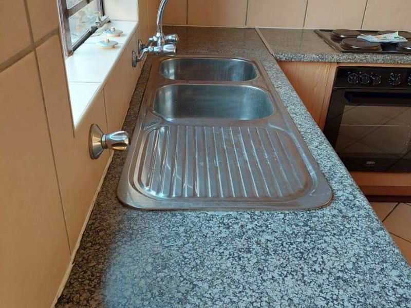 A functional kitchen area featuring granite countertops, a stainless steel double sink, and a built-in oven with an electric hob.