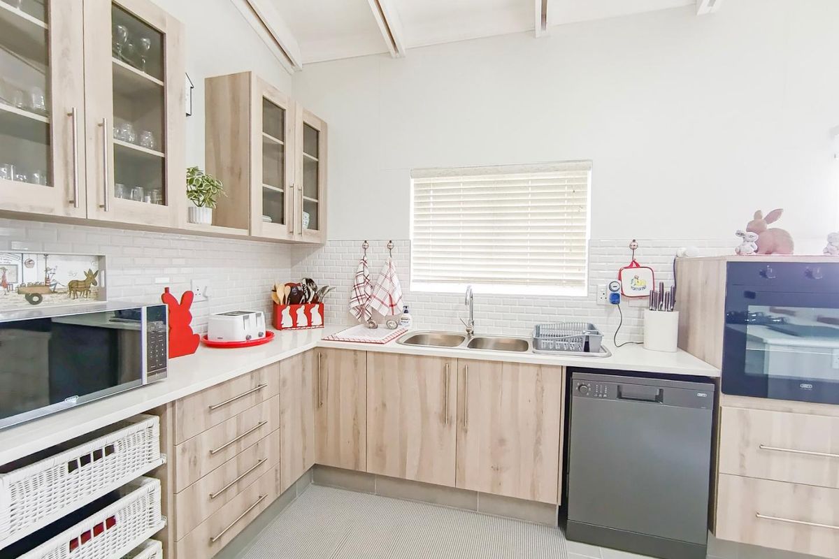 A well-maintained kitchen featuring light wood-grain cabinetry, white subway tile backsplash, integrated oven, and a double-basin sink with a window view.