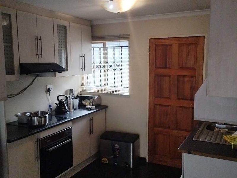 A functional kitchen featuring built-in cabinetry, an integrated oven, extractor fan, and dark tiled flooring with a wooden door leading to the exterior.