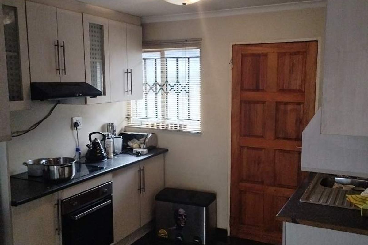 A functional kitchen featuring built-in cabinetry, an integrated oven, extractor fan, and dark tiled flooring with a wooden door leading to the exterior.