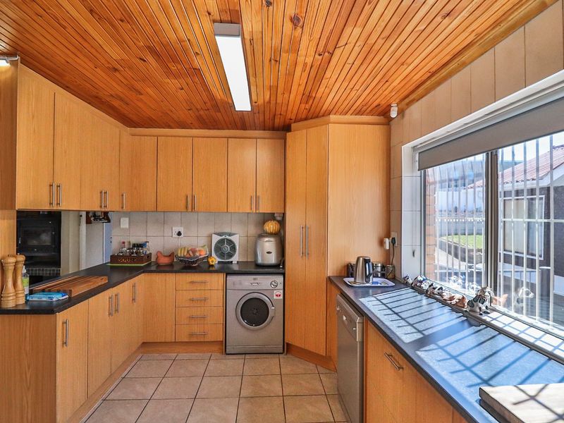 Functional kitchen featuring timber ceiling, laminate cabinetry, dark countertops, and integrated appliances, offering a practical layout with natural light.