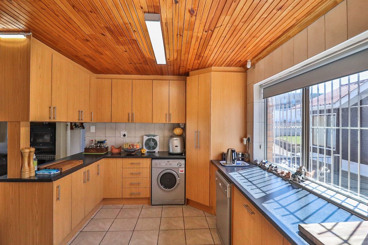 Functional kitchen featuring timber ceiling, laminate cabinetry, dark countertops, and integrated appliances, offering a practical layout with natural light.