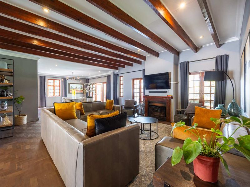 Spacious open-plan living area featuring exposed timber ceiling beams, elegant parquet flooring, and a cozy built-in fireplace with direct access to the outdoors.