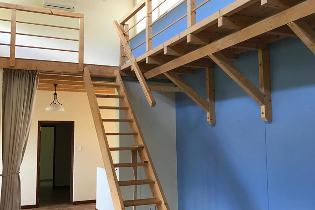 Spacious living area featuring a high timber-beamed ceiling, a mezzanine level with wooden railings, and a fixed wooden staircase.