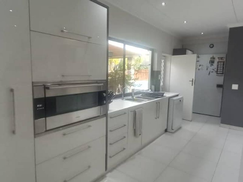 Modern kitchen featuring sleek white cabinetry, integrated oven and microwave, double sink, and tiled flooring with recessed lighting.