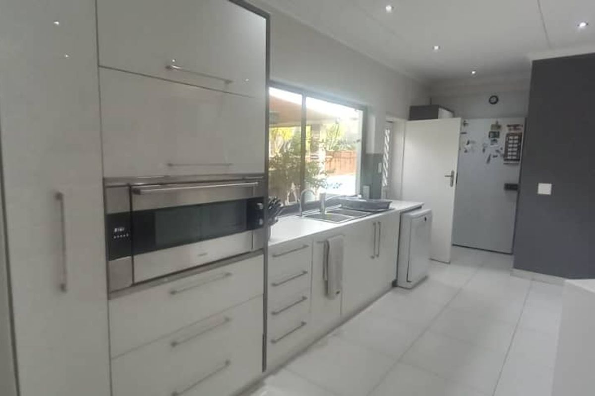 Modern kitchen featuring sleek white cabinetry, integrated oven and microwave, double sink, and tiled flooring with recessed lighting.