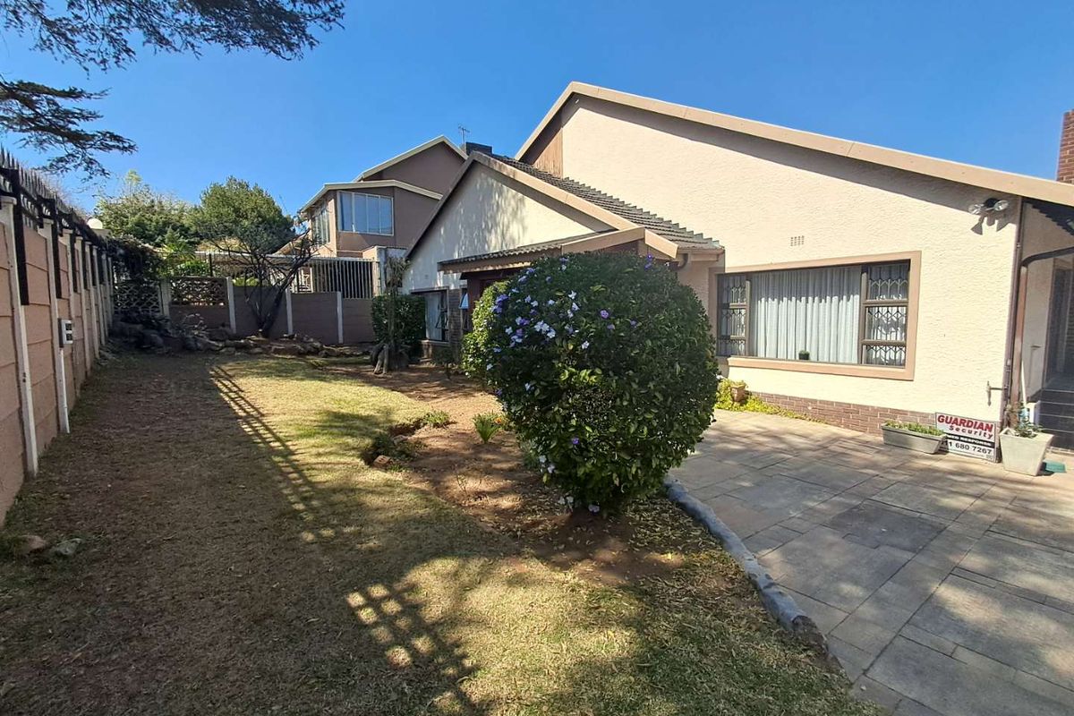 Rear exterior view of the house featuring a paved patio area, lawn, and perimeter walling with security features.