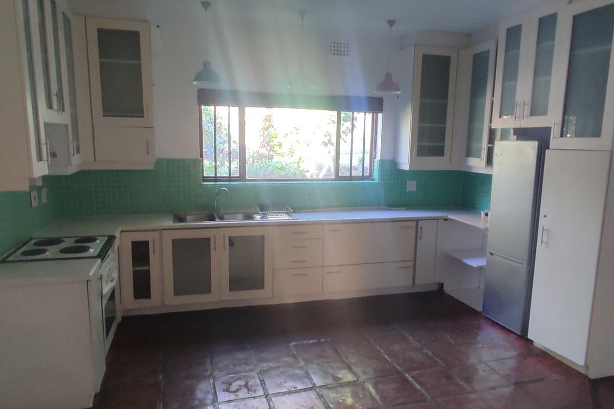 A functional kitchen featuring white cabinetry, a green tiled backsplash, built-in oven and hob, and terracotta-style floor tiles with natural light.