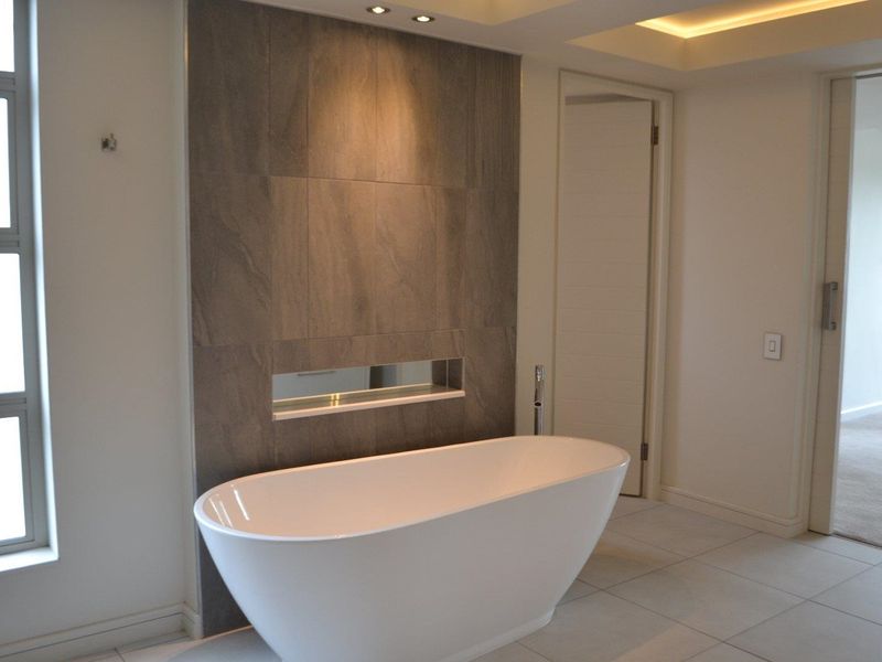 Modern bathroom featuring a sleek freestanding bathtub, a tiled feature wall with a recessed niche, and elegant recessed ceiling and cove lighting.