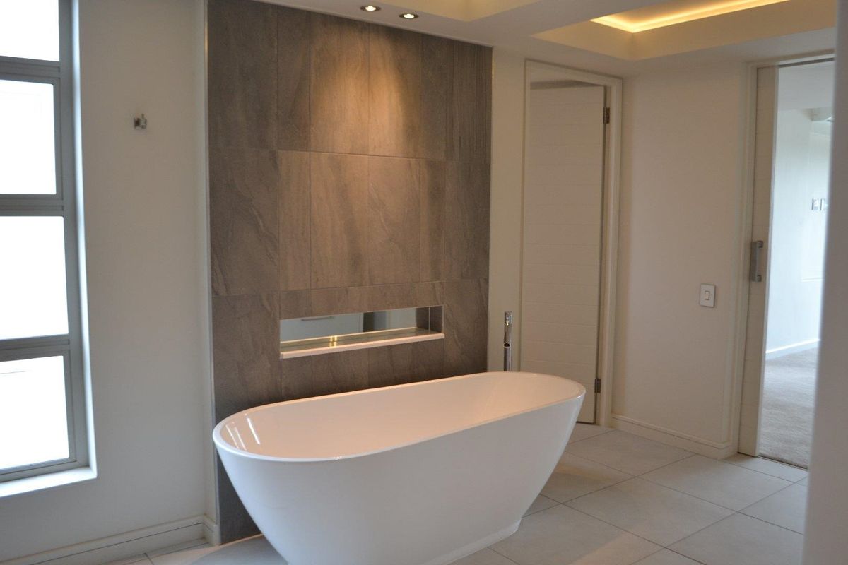 Modern bathroom featuring a sleek freestanding bathtub, a tiled feature wall with a recessed niche, and elegant recessed ceiling and cove lighting.