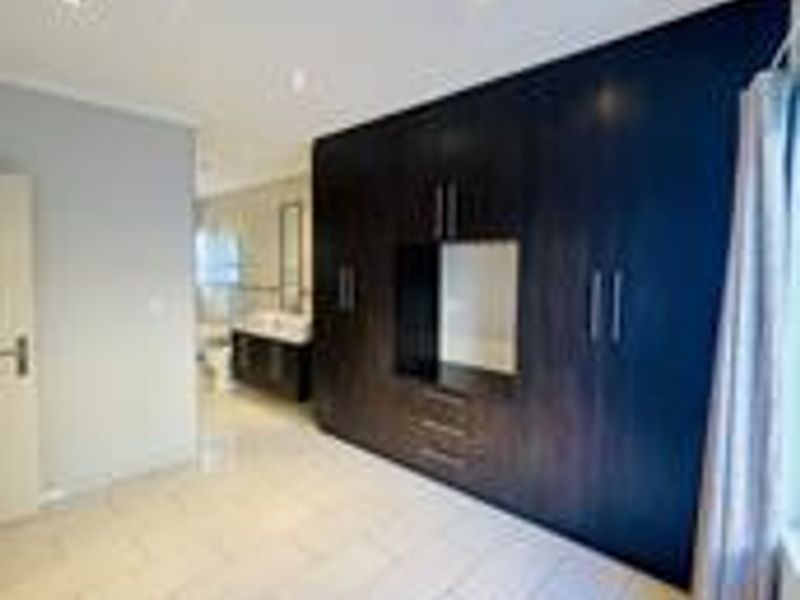Spacious bedroom featuring extensive dark wood built-in cupboards, neutral tiled flooring, and recessed lighting, with an adjoining en-suite bathroom visible.