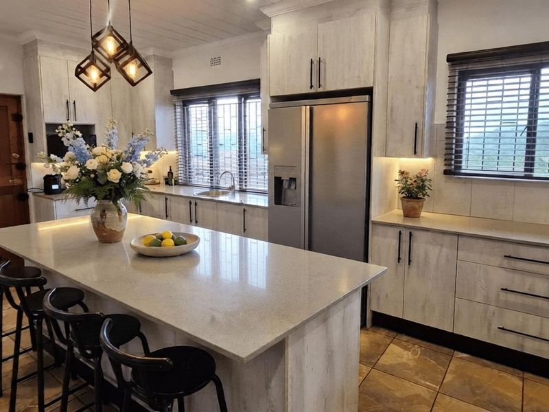 Modern kitchen featuring a large central island with stone countertops, ample built-in cabinetry, integrated appliances, and tiled flooring with warm under-cabinet lighting.