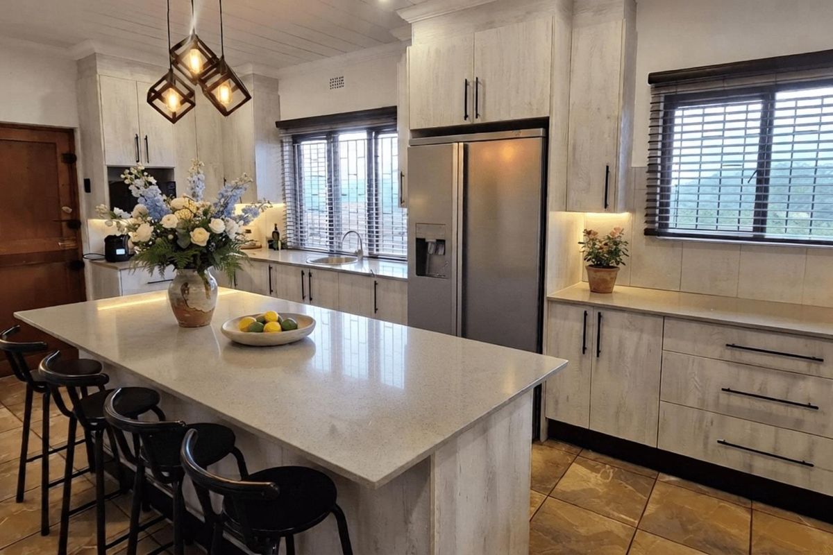 Modern kitchen featuring a large central island with stone countertops, ample built-in cabinetry, integrated appliances, and tiled flooring with warm under-cabinet lighting.