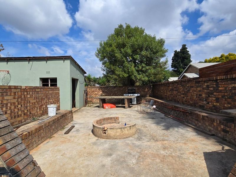 Spacious rear courtyard featuring a built-in fire pit, concrete seating areas, and brick boundary walls, offering potential for an outdoor entertainment space.