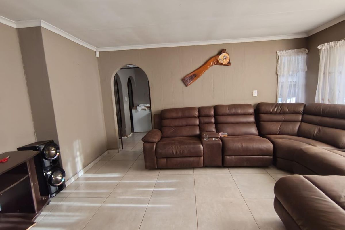A spacious living room featuring neutral tiled flooring, an arched doorway leading to adjacent rooms, and large windows allowing natural light.