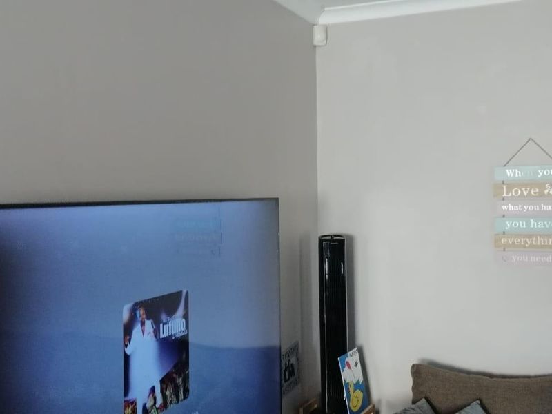 A corner view of a living room featuring neutral wall paint, coving, and a mounted alarm sensor.