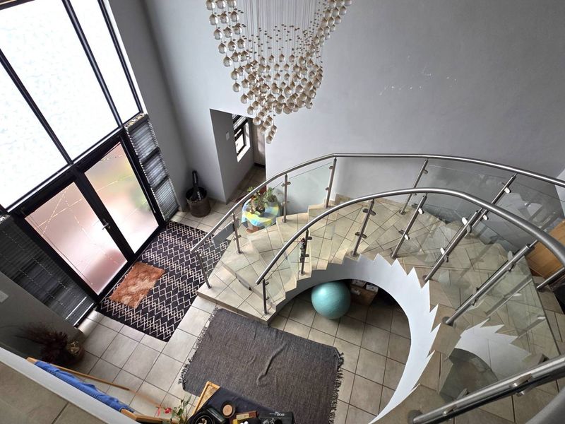 Spacious double-volume entrance hall featuring a striking curved staircase with glass balustrades, large windows, and a decorative chandelier.