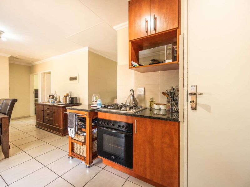 Compact kitchen area featuring wooden cabinetry, granite countertops, a gas hob, and a built-in oven, seamlessly flowing into the adjacent dining space.