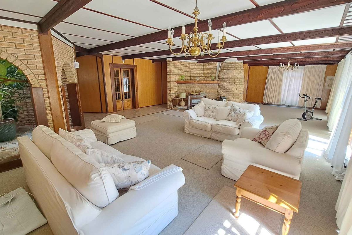 Spacious living area featuring exposed timber ceiling beams, a prominent brick fireplace, and large windows allowing for ample natural light.