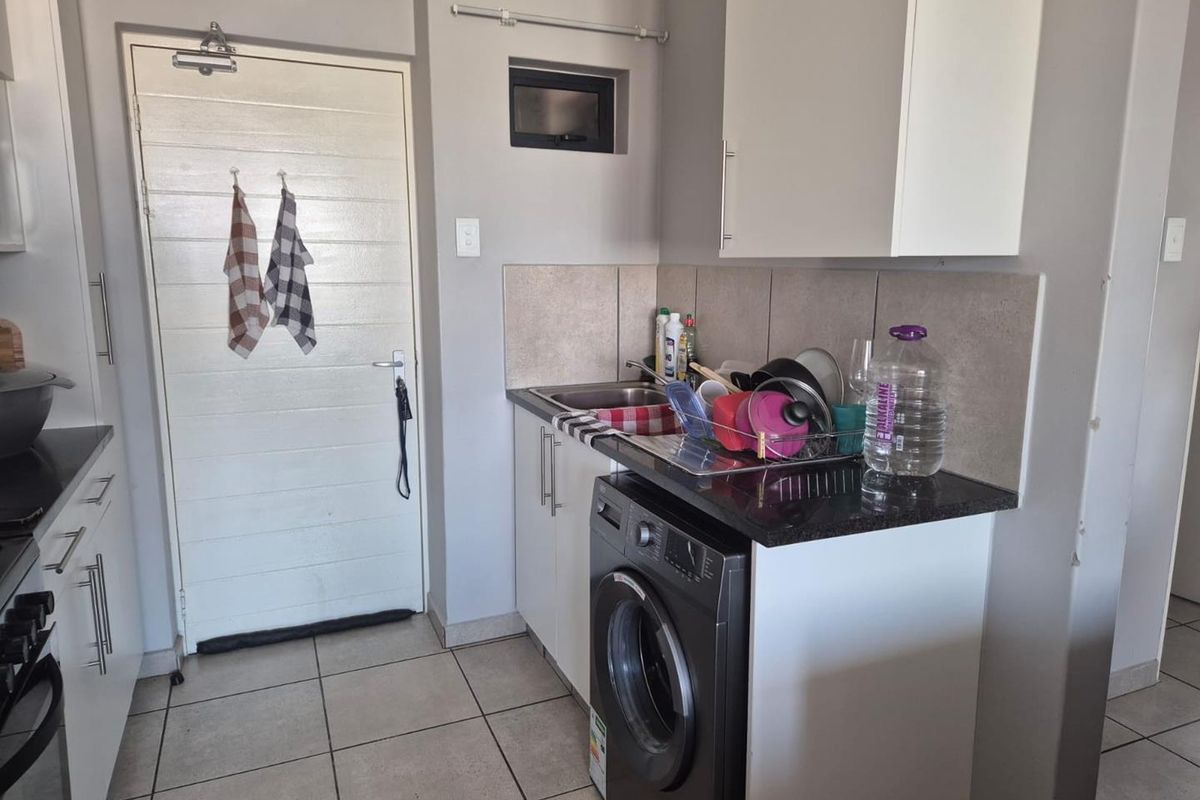 A functional kitchen area featuring built-in cabinetry, a granite countertop, a stainless steel sink, and space for a front-loading washing machine.