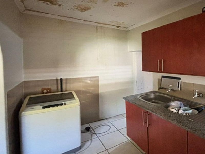 A laundry area featuring built-in cabinetry, a stainless steel sink, and tiled flooring, currently showing significant signs of ceiling water damage.