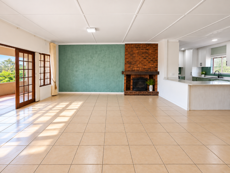 Spacious open-plan living area featuring a brick fireplace, tiled flooring, and seamless flow to an outdoor patio, adjacent to a modern kitchen.