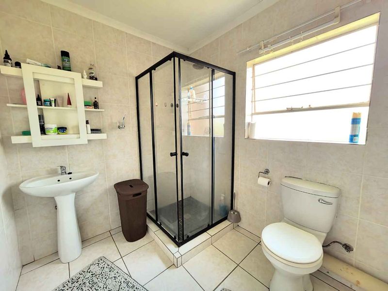 A functional bathroom featuring a corner shower enclosure, pedestal basin, toilet, and neutral wall and floor tiling.