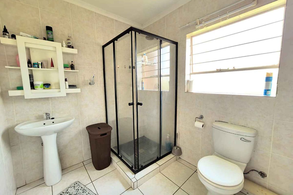A functional bathroom featuring a corner shower enclosure, pedestal basin, toilet, and neutral wall and floor tiling.