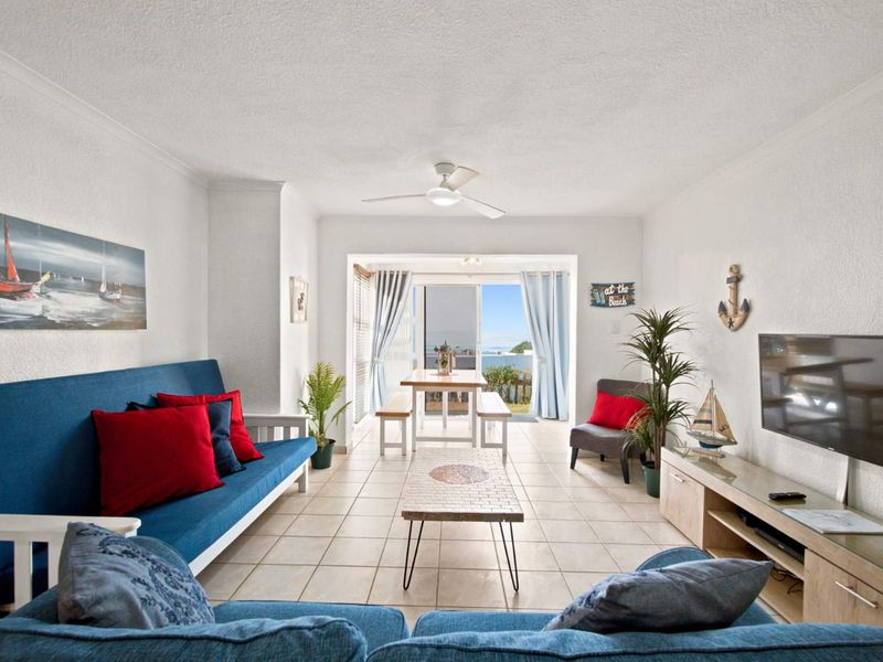 Bright open-plan living and dining area featuring tiled floors, a ceiling fan, and sliding glass doors leading to an outdoor space with coastal views.